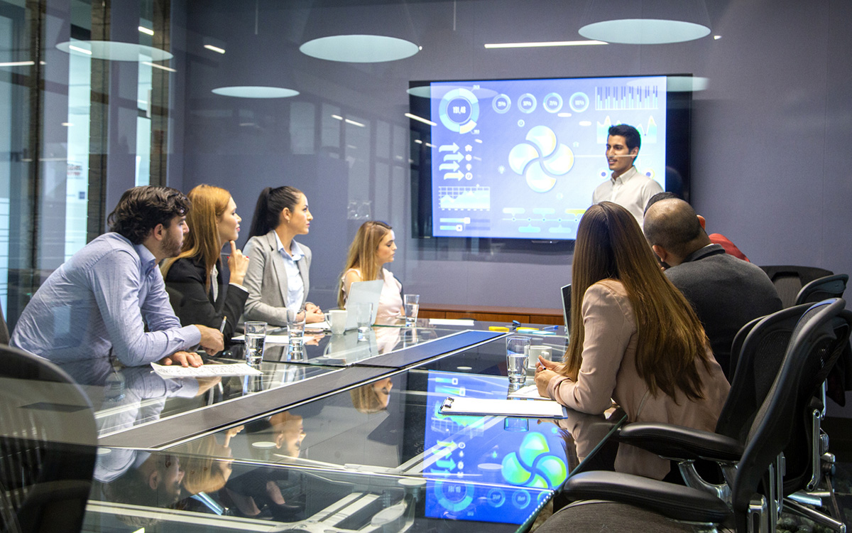A team presenting data charts on a screen in a glass conference room