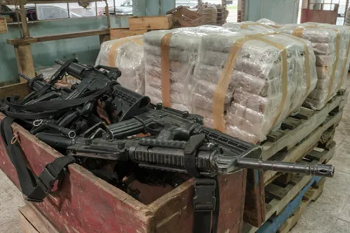 Seized guns and wrapped drug bundles stacked on pallets