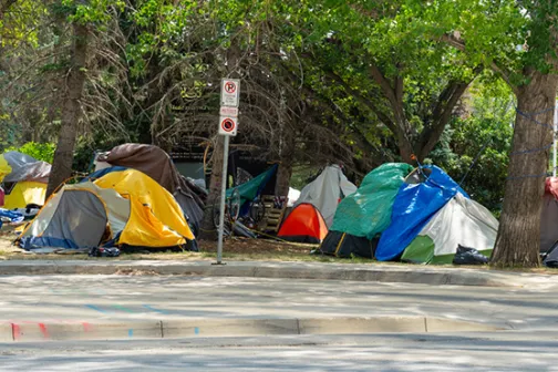 A row of tents in a homeless encampment along a city sidewalk